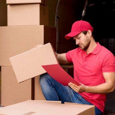 Repartidor con gorra y polo rojos revisa el albarán junto a las cajas apiladas en la furgoneta de reparto de mercancías